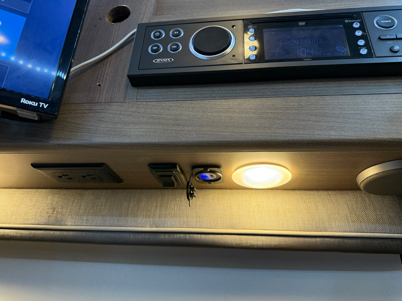 RV rental interior featuring a Roku TV, Jensen stereo, AC/USB outlets, speaker, and light for onboard entertainment and charging.