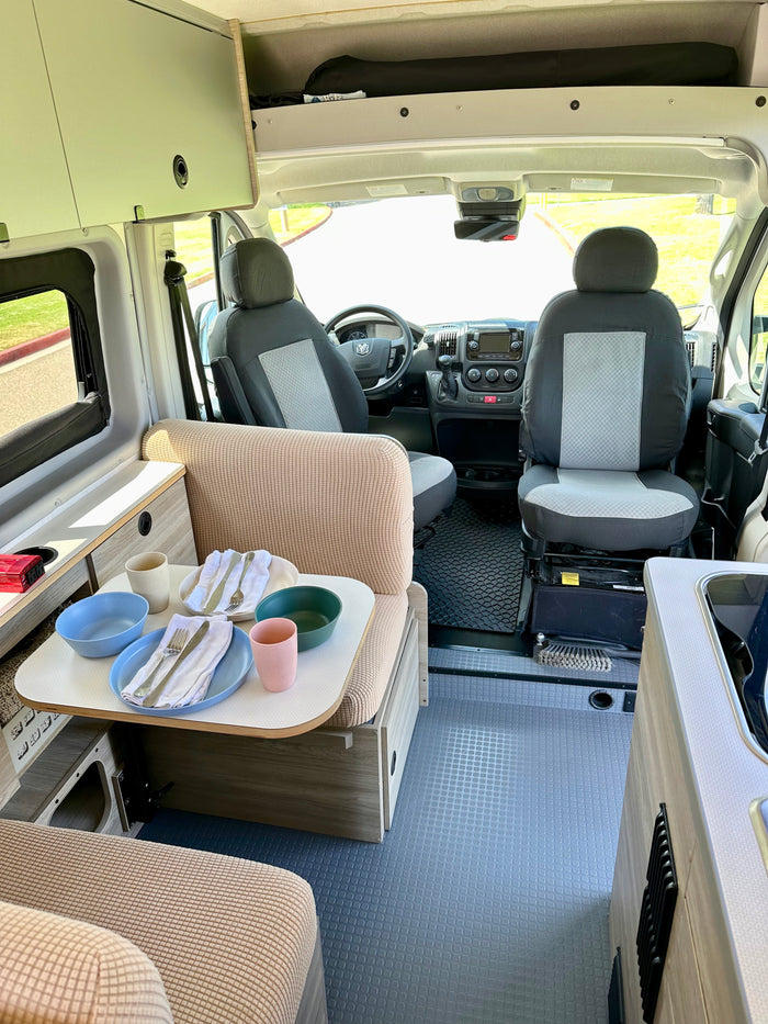 This clean rv rental interior offers a dining table with place settings, comfortable seating, and the full cockpit view.