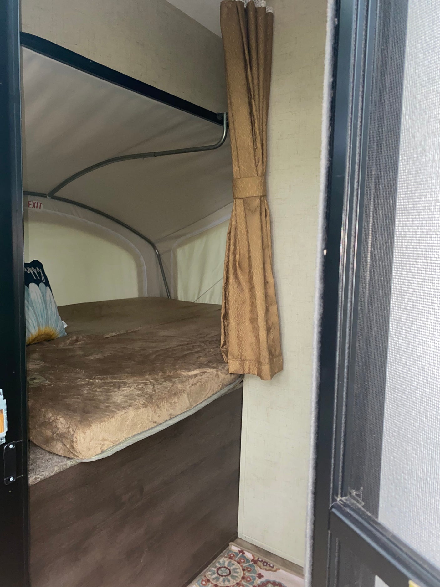 Inside an RV rental pop-up camper, showing the bed, soft mattress, and cozy interior space with a curtain and exit sign.