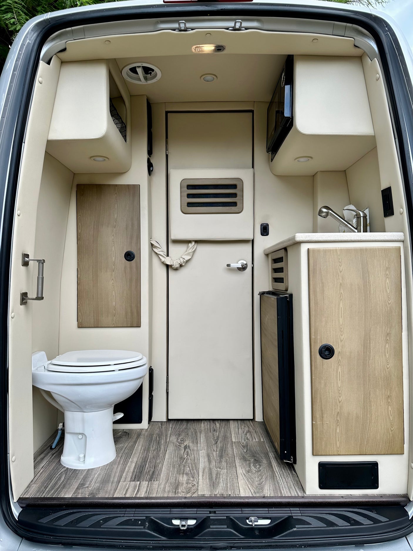RV rental: Compact camper van interior featuring toilet, kitchenette with sink, microwave, fridge, and stylish wood-look accents.