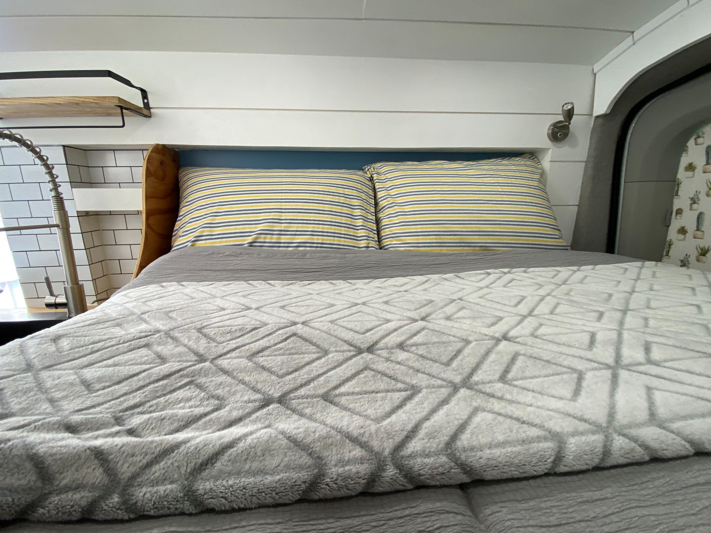 Cozy RV rental interior: A comfy bed with striped pillows, adjacent to a functional kitchen sink & shiplap walls.