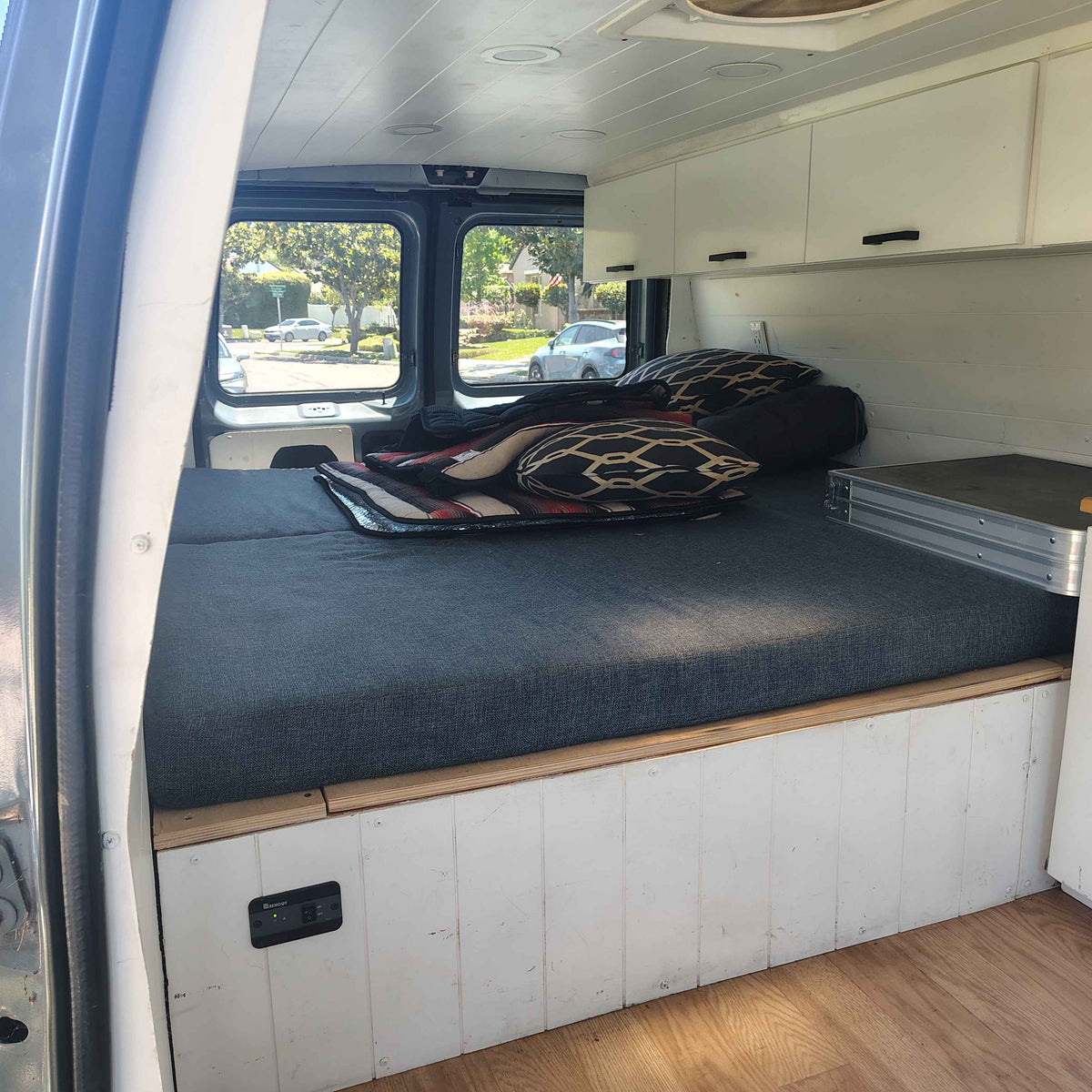 RV rental camper van's interior. Features a large bed, overhead cabinets, planked ceiling, wood floor, and Renogy switch. — photo 6