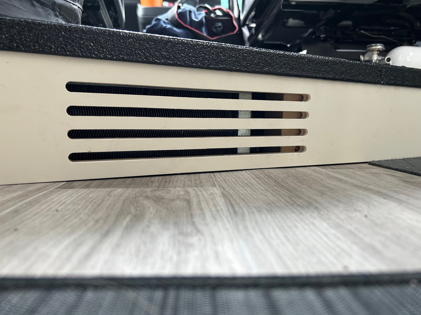 Up-close RV rental interior: white panel with climate control vents, black textured step, and wood-look floor.