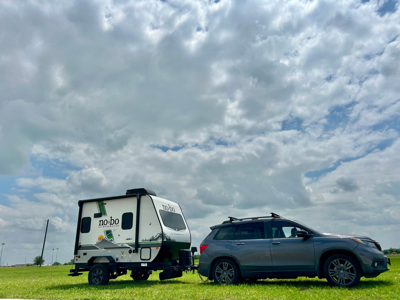 Grey SUV towing a "No Boundaries" travel trailer, perfect for your next RV rental adventure or camping trip under cloudy skies.