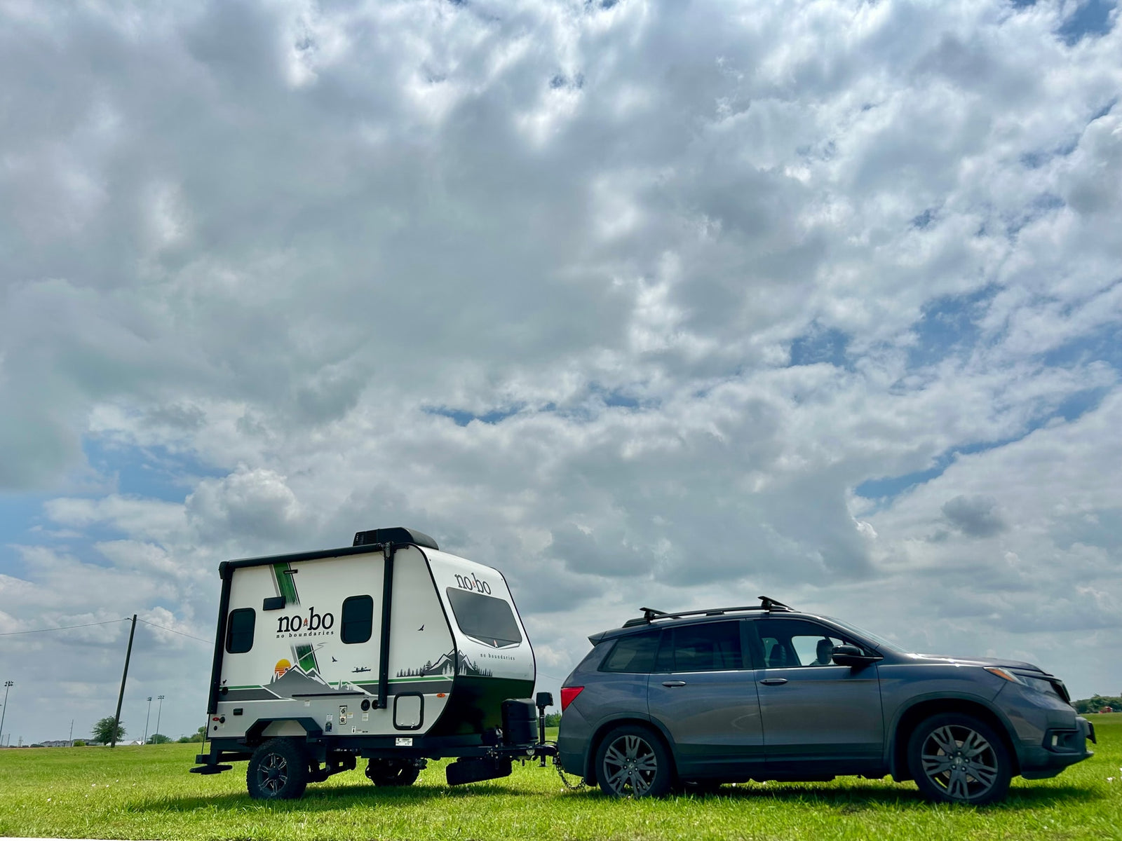 Grey SUV towing a "No Boundaries" travel trailer, perfect for your next RV rental adventure or camping trip under cloudy skies.