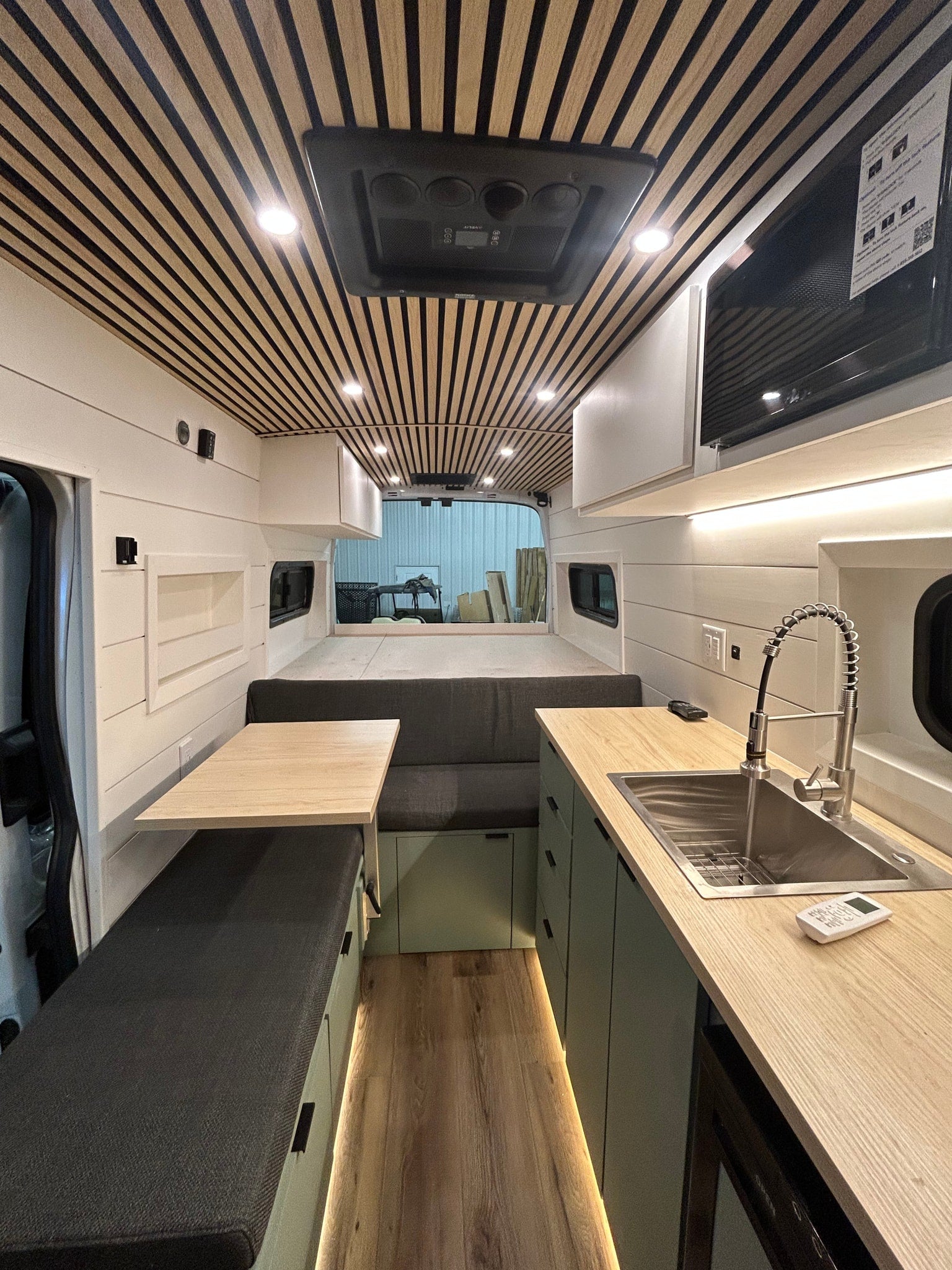 This modern rv rental camper van interior boasts a well-equipped kitchenette, modular bed, and striking wood-slat ceiling.