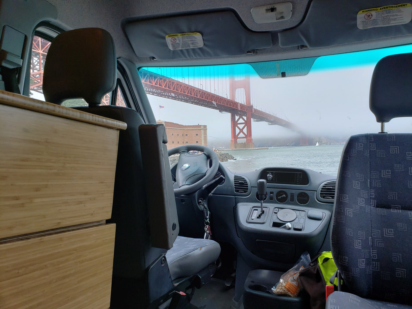 Inside an RV rental, a stunning view of the Golden Gate Bridge emerges from the fog over the bay, as seen from the driver's seat.