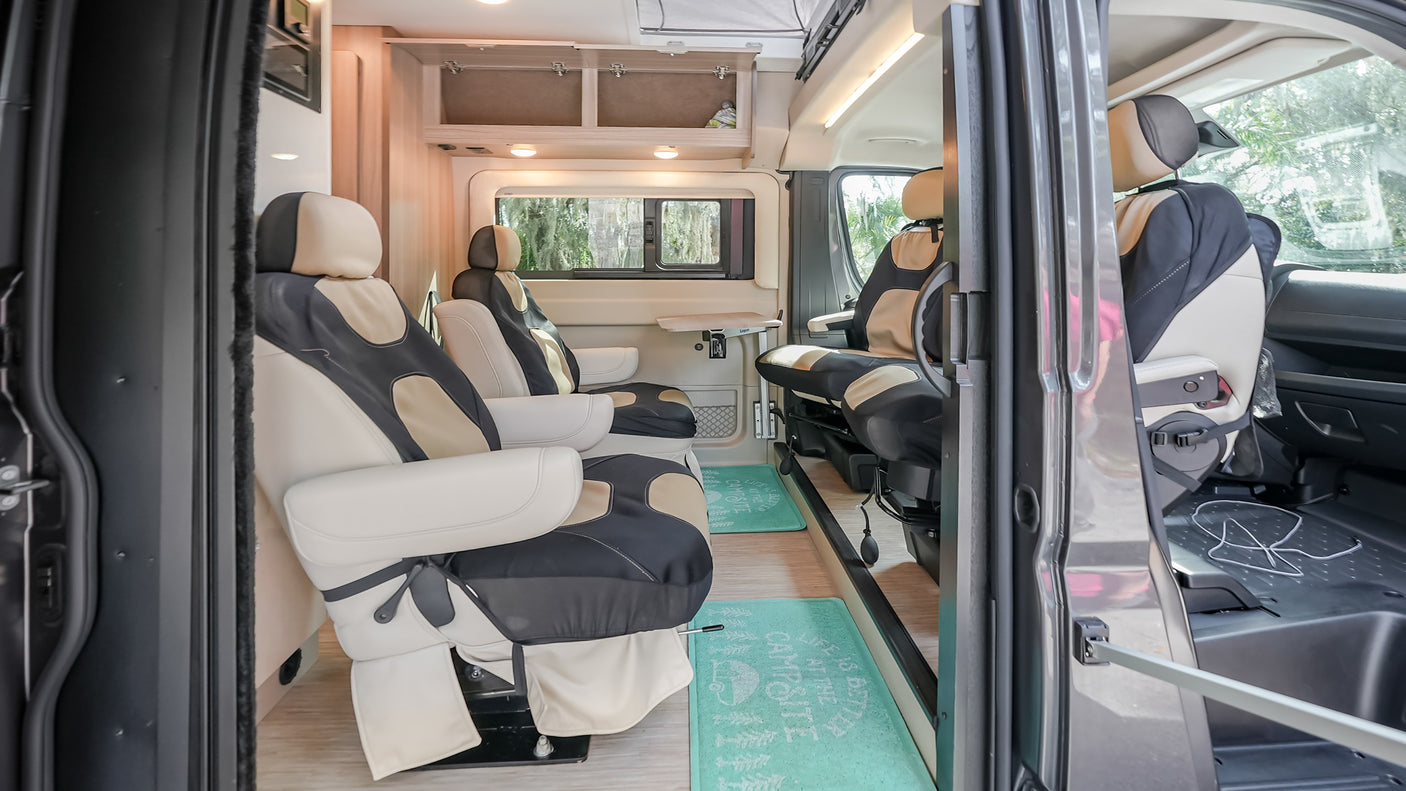 Spacious RV rental interior with cream/black swivel seats, wooden cabinetry, and floor mats, ready for comfortable travel adventures.