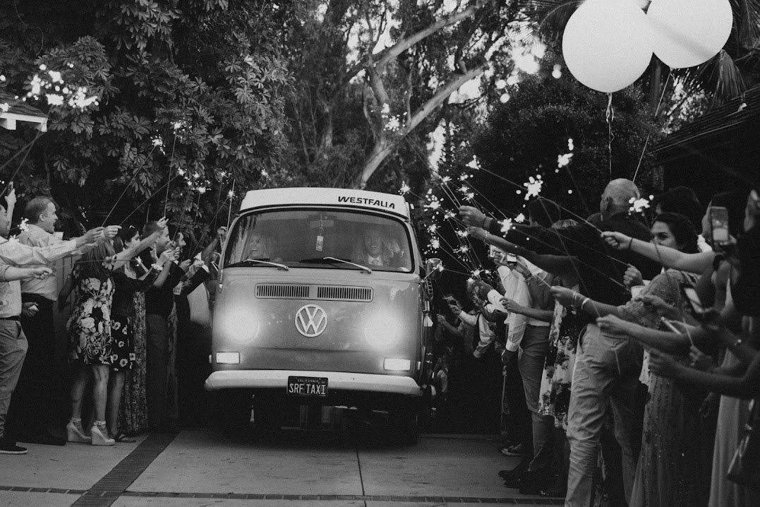 Black and white photo of a vintage Westfalia RV rental carrying a couple, surrounded by guests with sparklers. — photo 15