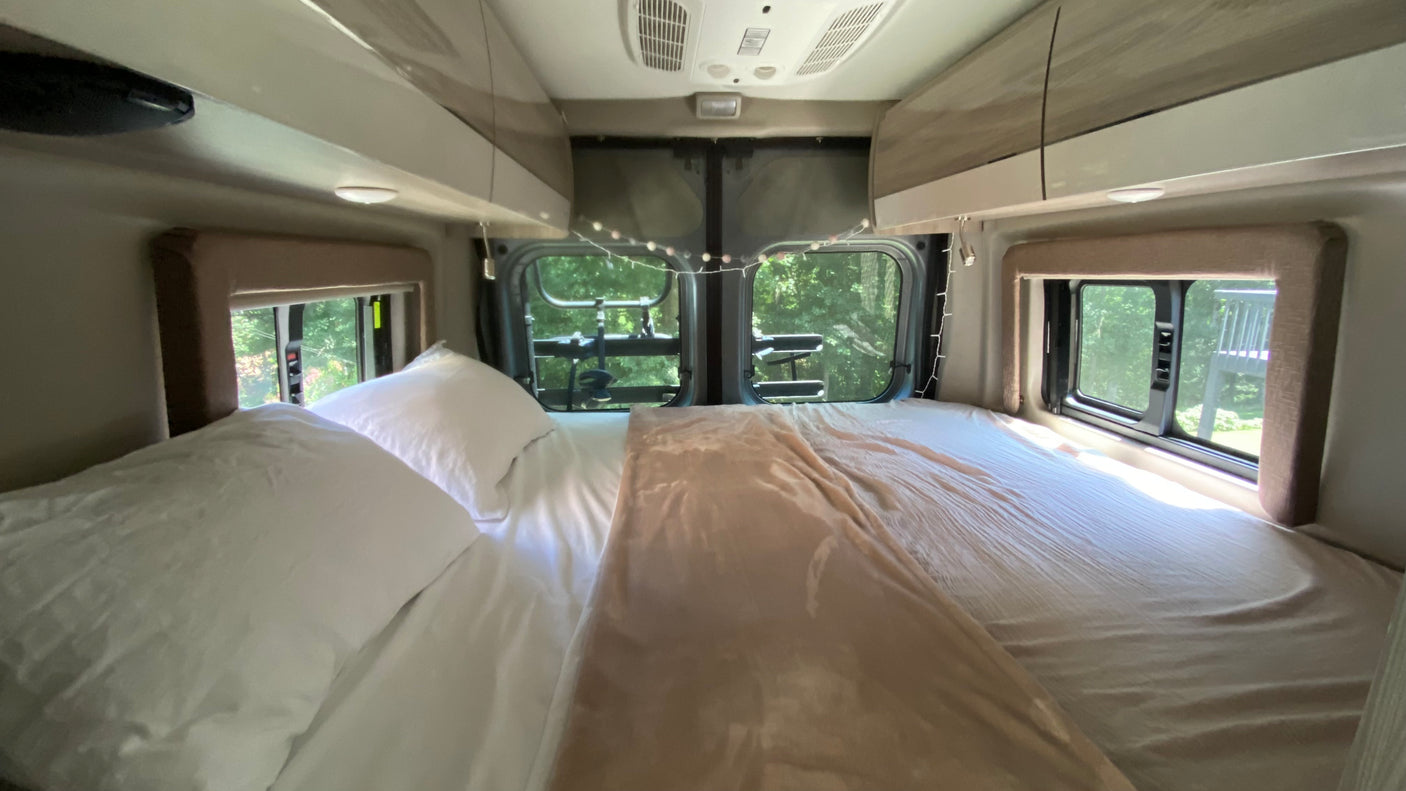 Cozy RV rental interior: a comfy bed with soft linens, windows offering natural views, and charming string lights.