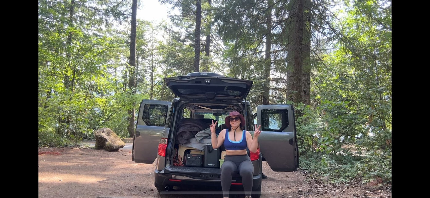 A woman relaxes in her car camping SUV, packed with gear. A perfect RV rental alternative for forest adventures.