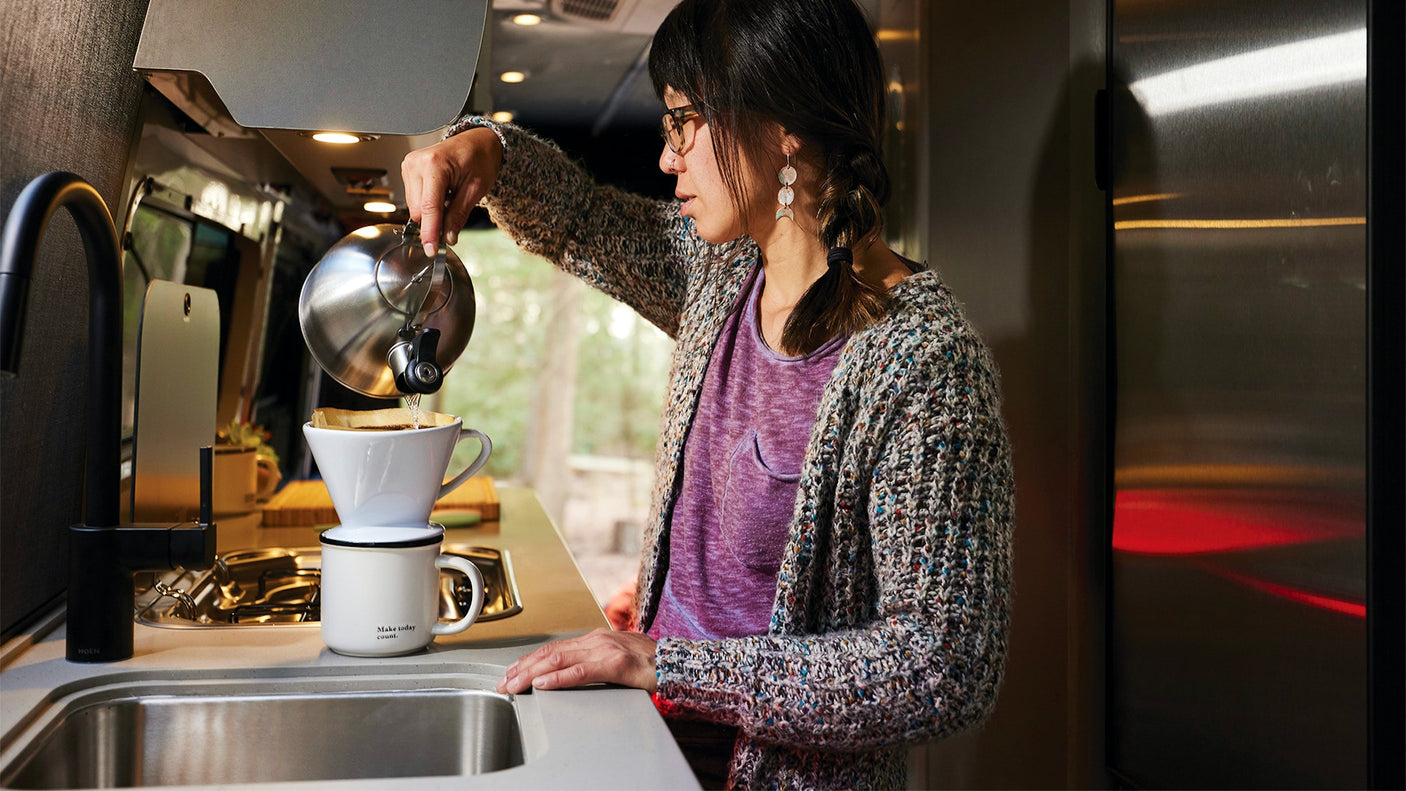 Start your day right! A woman makes fresh pour-over coffee in a compact RV rental kitchen.