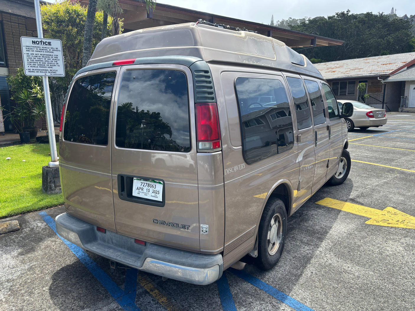 A tan Chevrolet Discovery passenger van (potential RV rental) parked in a lot with a visible notice sign.