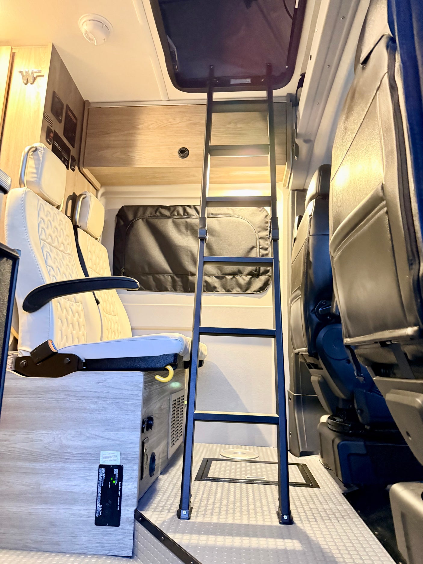 This RV rental interior features a sturdy bunk ladder, passenger seats, and essential camper van systems.