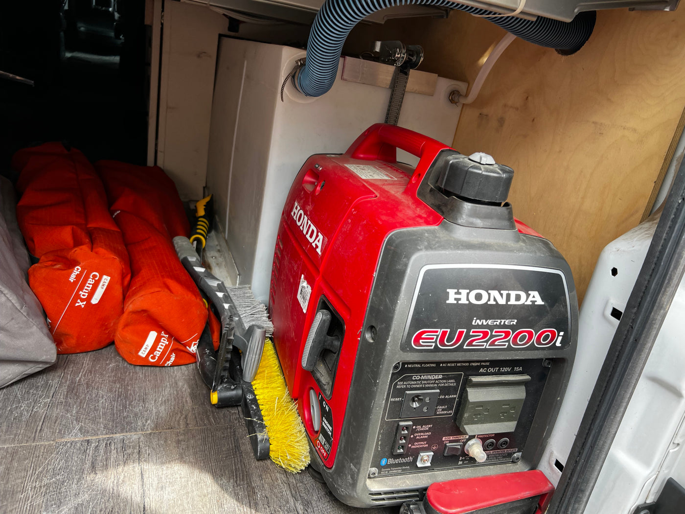 Essential gear in an RV rental: Honda inverter generator, CampX chairs, and cleaning brush stored in the cargo area. — photo 13