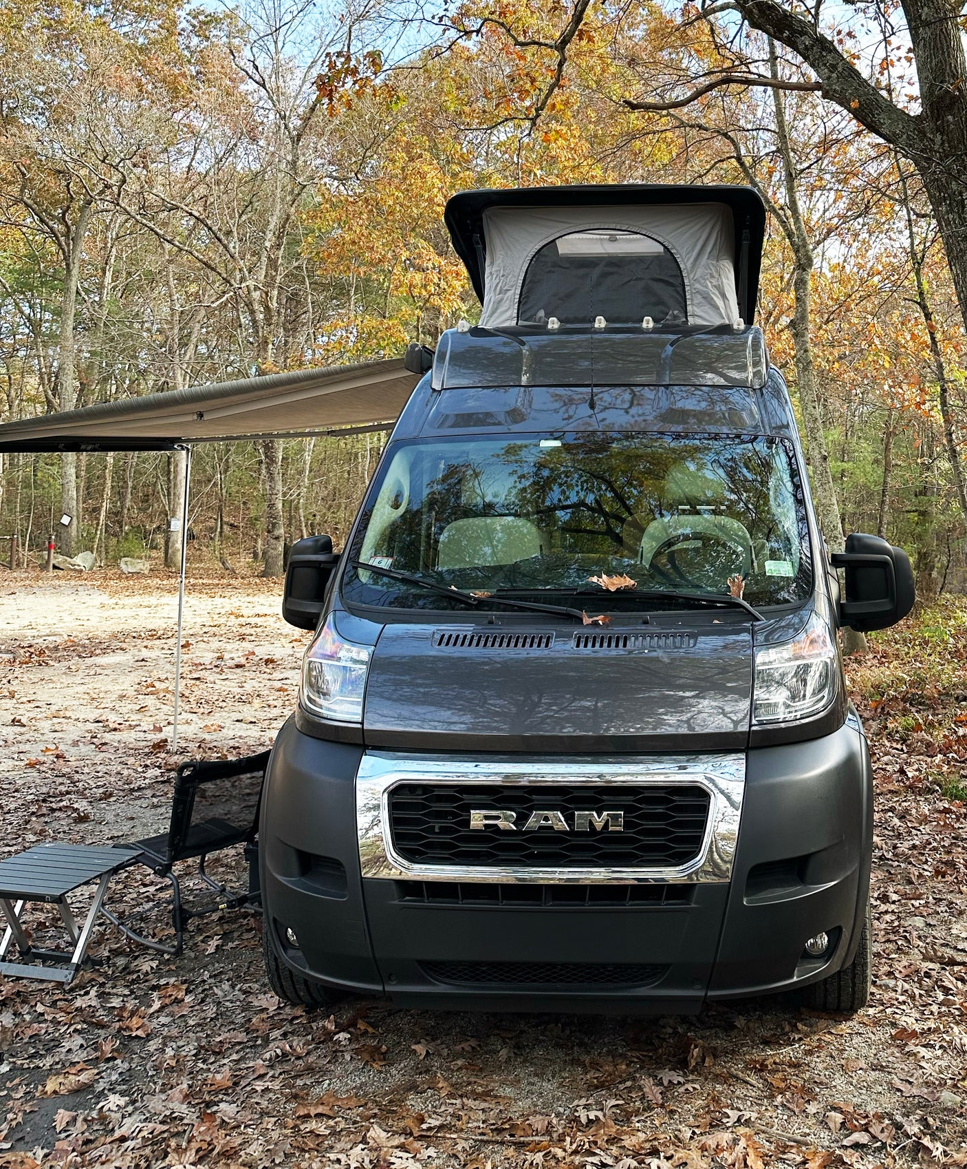 An RV rental camper van with pop-top and awning, parked at a fall campsite amidst colorful autumn leaves.