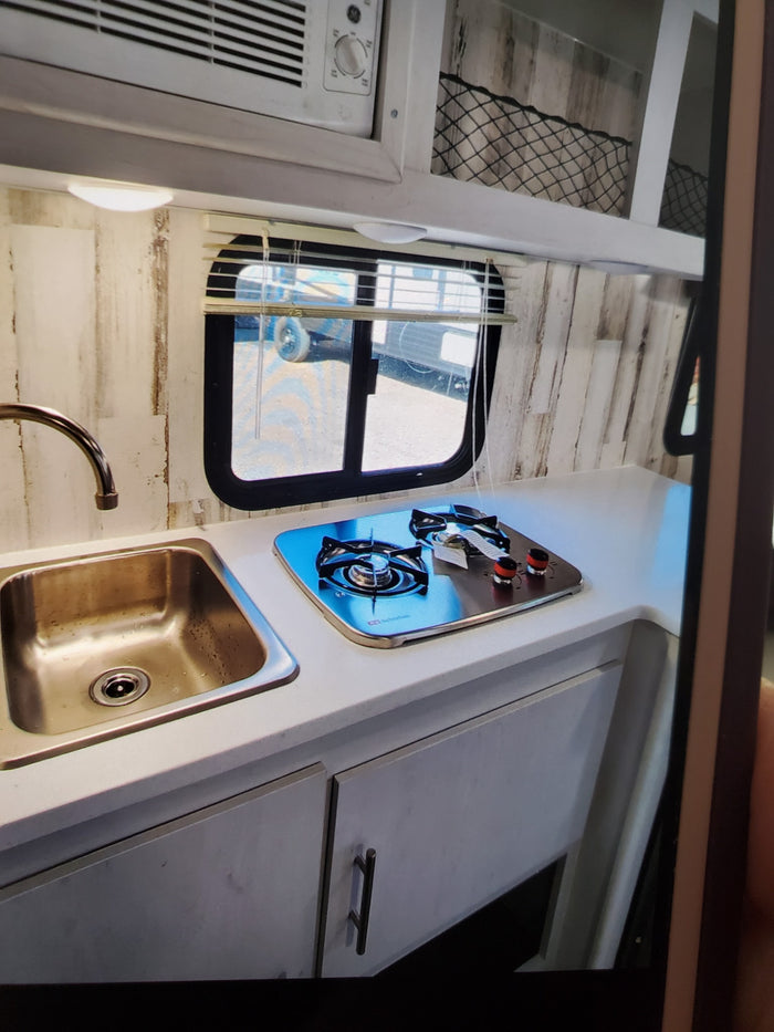 Compact RV rental kitchen with sink, gas cooktop, and rustic wood-paneled walls, perfect for travel.