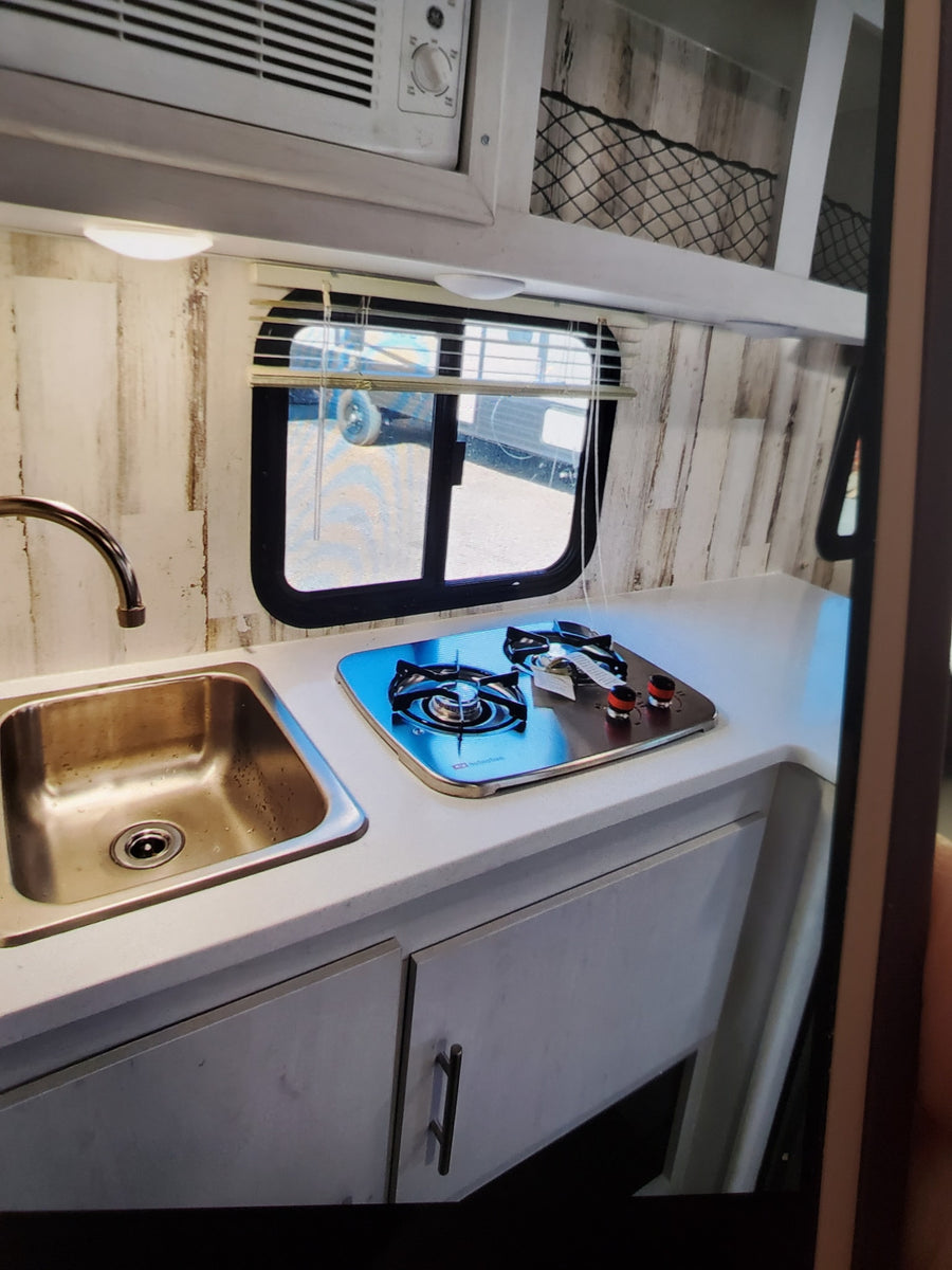 Compact RV rental kitchen with sink, gas cooktop, and rustic wood-paneled walls, perfect for travel.