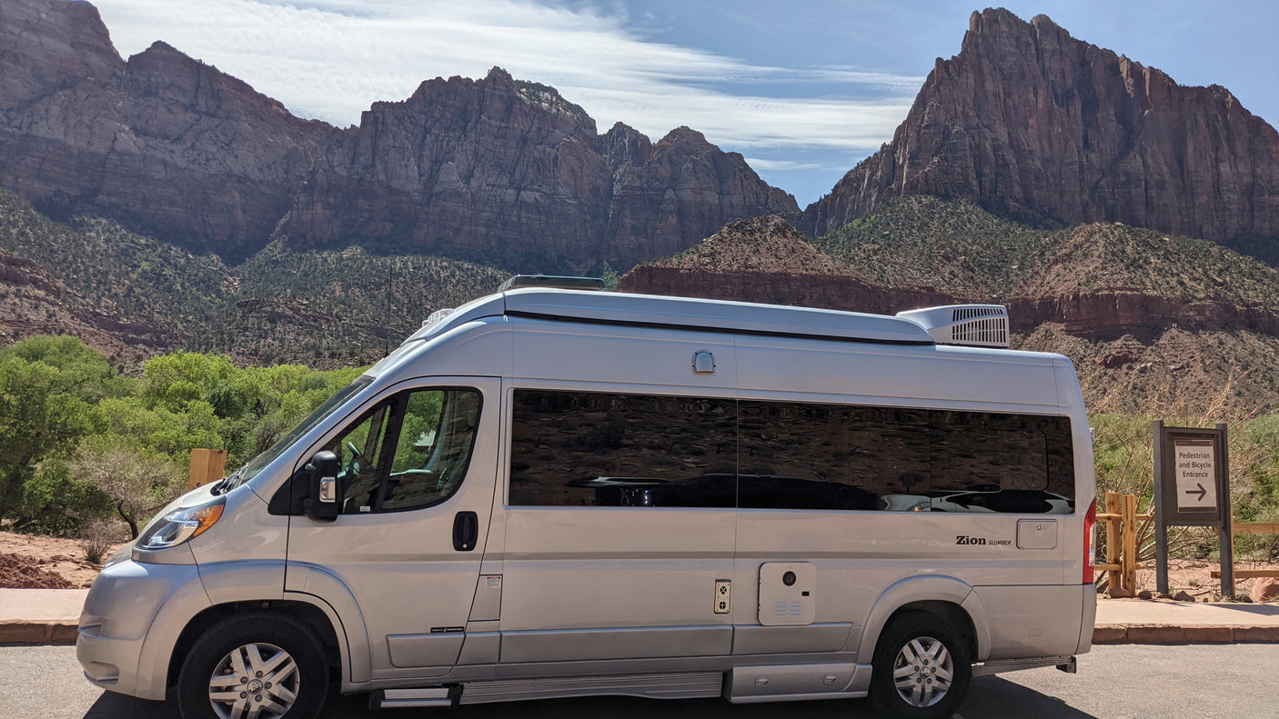 An RV rental camper van is parked against a backdrop of majestic mountains and a blue sky in Zion National Park.