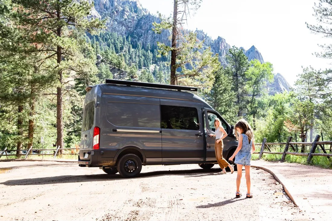 Experience nature with an RV rental! A woman and girl exit their camper van in a beautiful mountain park setting.