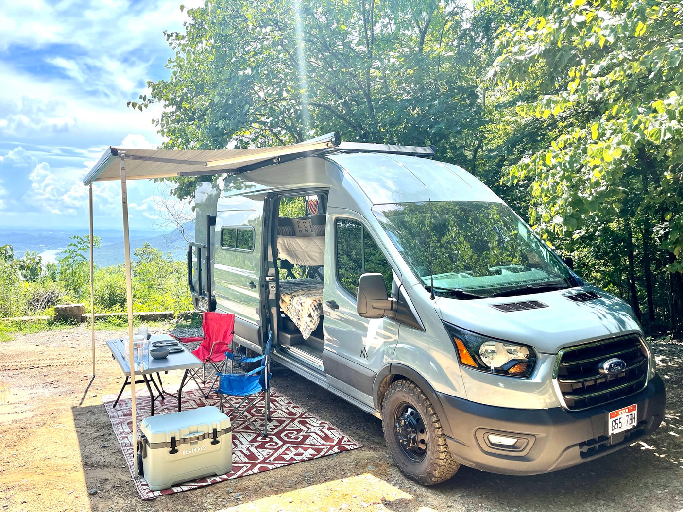 A silver Ford Transit RV rental with an awning and full outdoor camping setup, enjoying a beautiful mountain view.