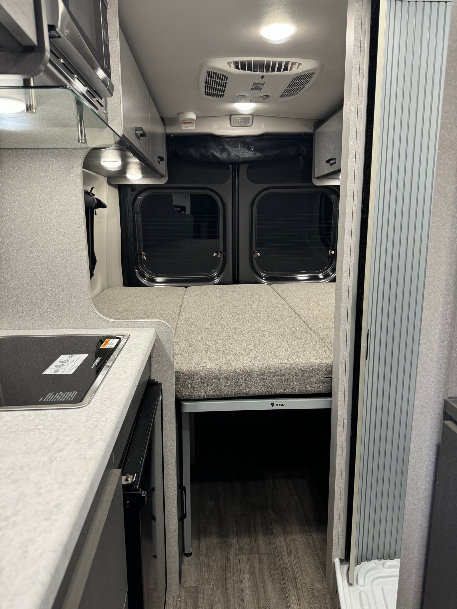View inside an RV rental featuring a Dometic cooktop, Thor bed setup, and modern camper van interior details.