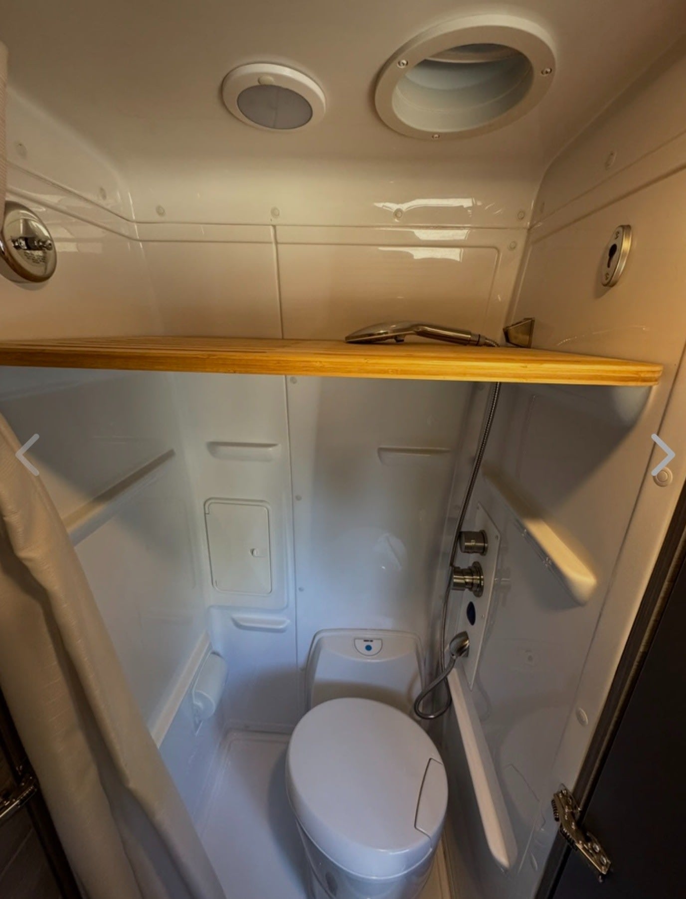 Compact RV rental wet bath features a toilet, shower, and convenient storage shelf. Ideal for space-saving.