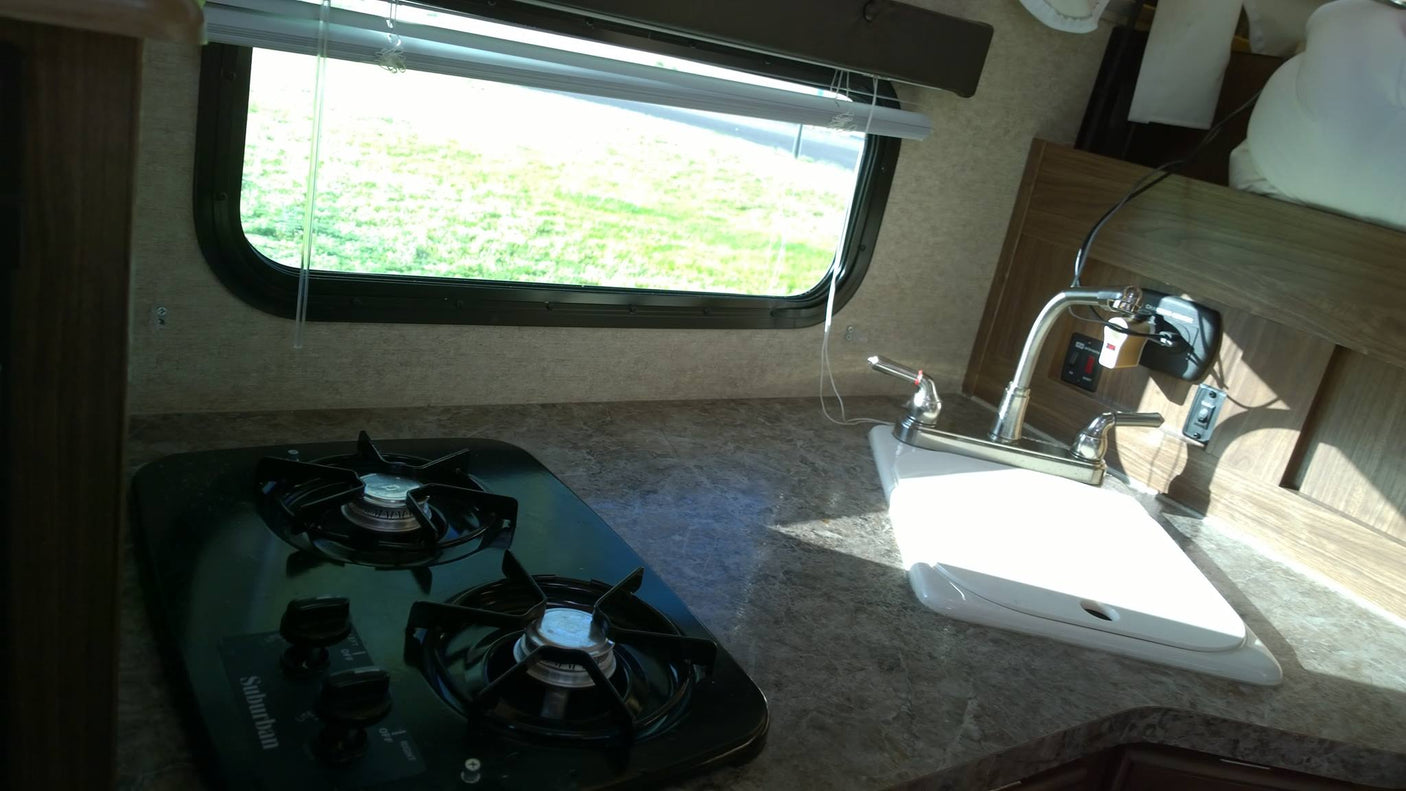 ready for an RV rental outdoor adventure among bare trees and hills.|Palomino truck camper RV rental on a white Nissan truck at a forest lakeside campsite with kayaks.|RV rental: Compact kitchenette with a two-burner Suburban gas stovetop
