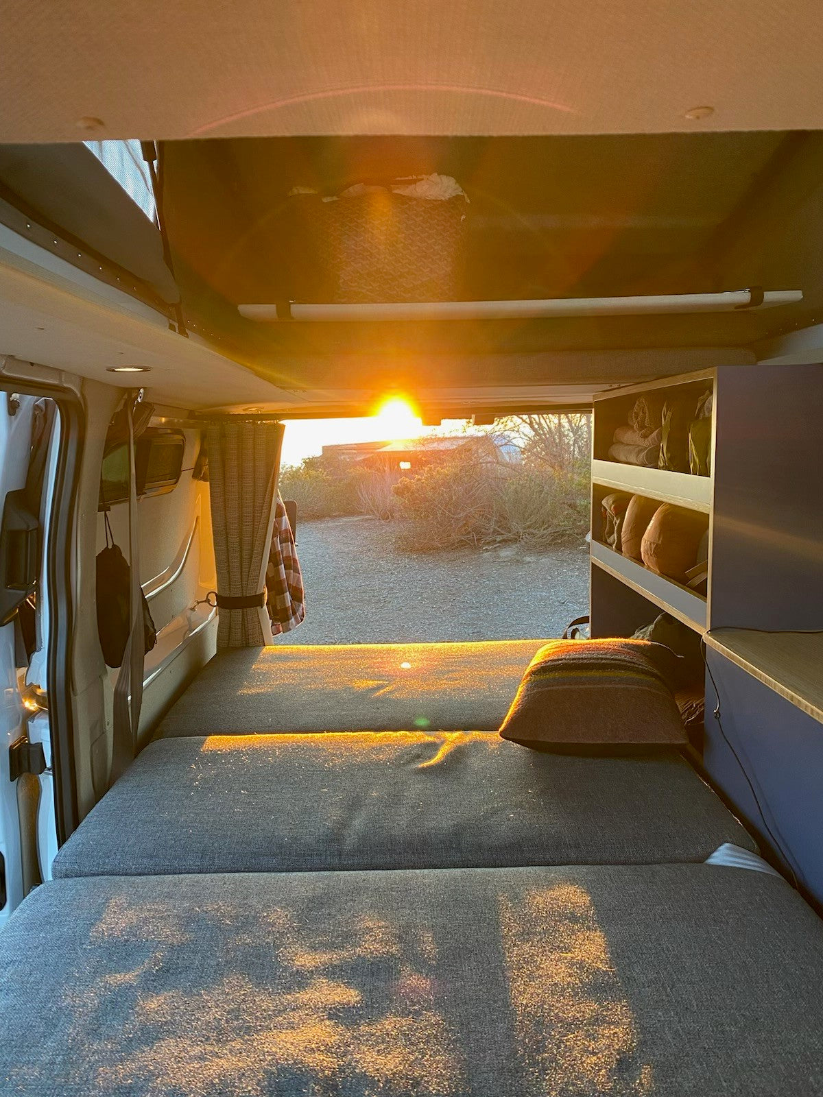 Golden light floods this cozy RV rental interior. Sunset over sparse landscape from van's open rear, with a bed & shelves. — photo 4