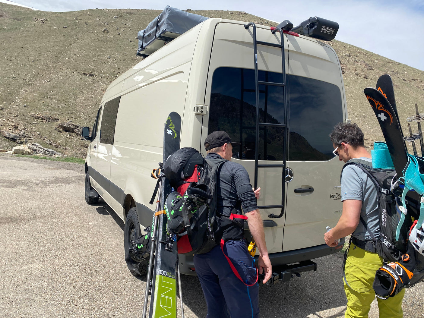 Two men with backcountry ski gear prepare by their Mercedes Sprinter **rv rental** van, ready for mountain adventures.