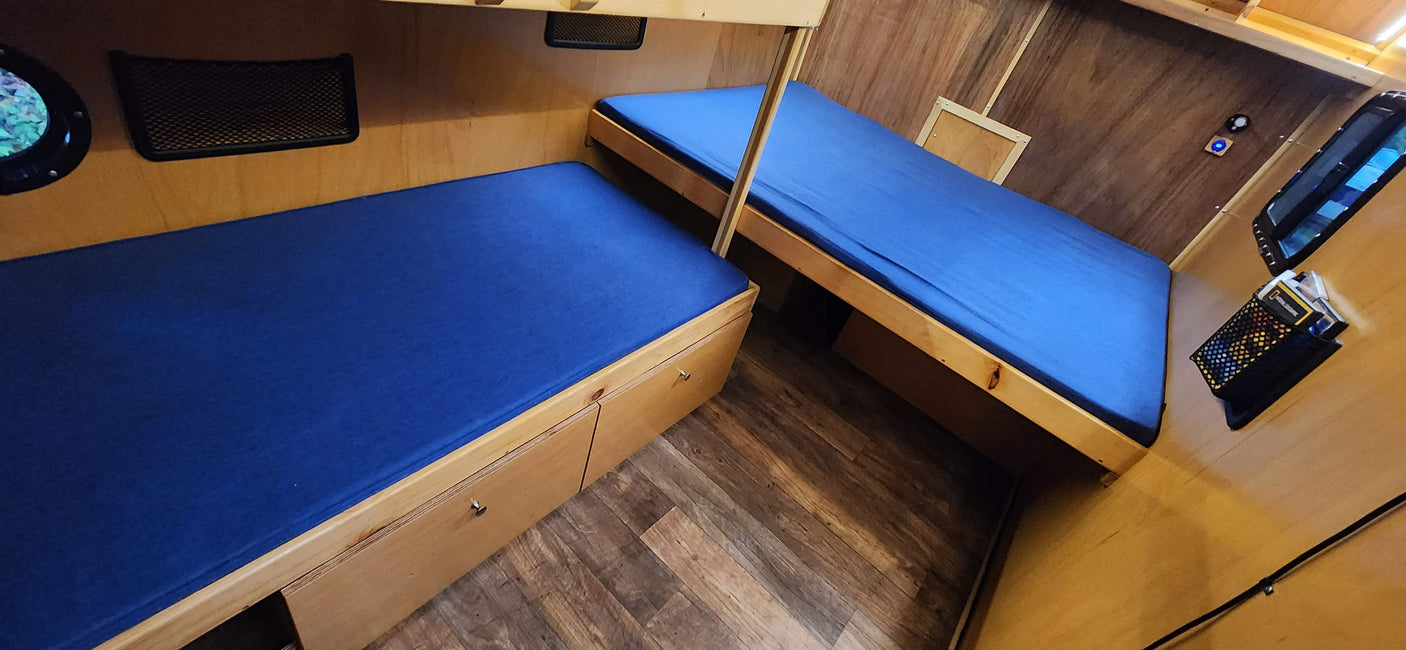 Cozy RV rental interior with two compact bunk beds featuring blue mattresses, wooden paneling, and built-in storage.