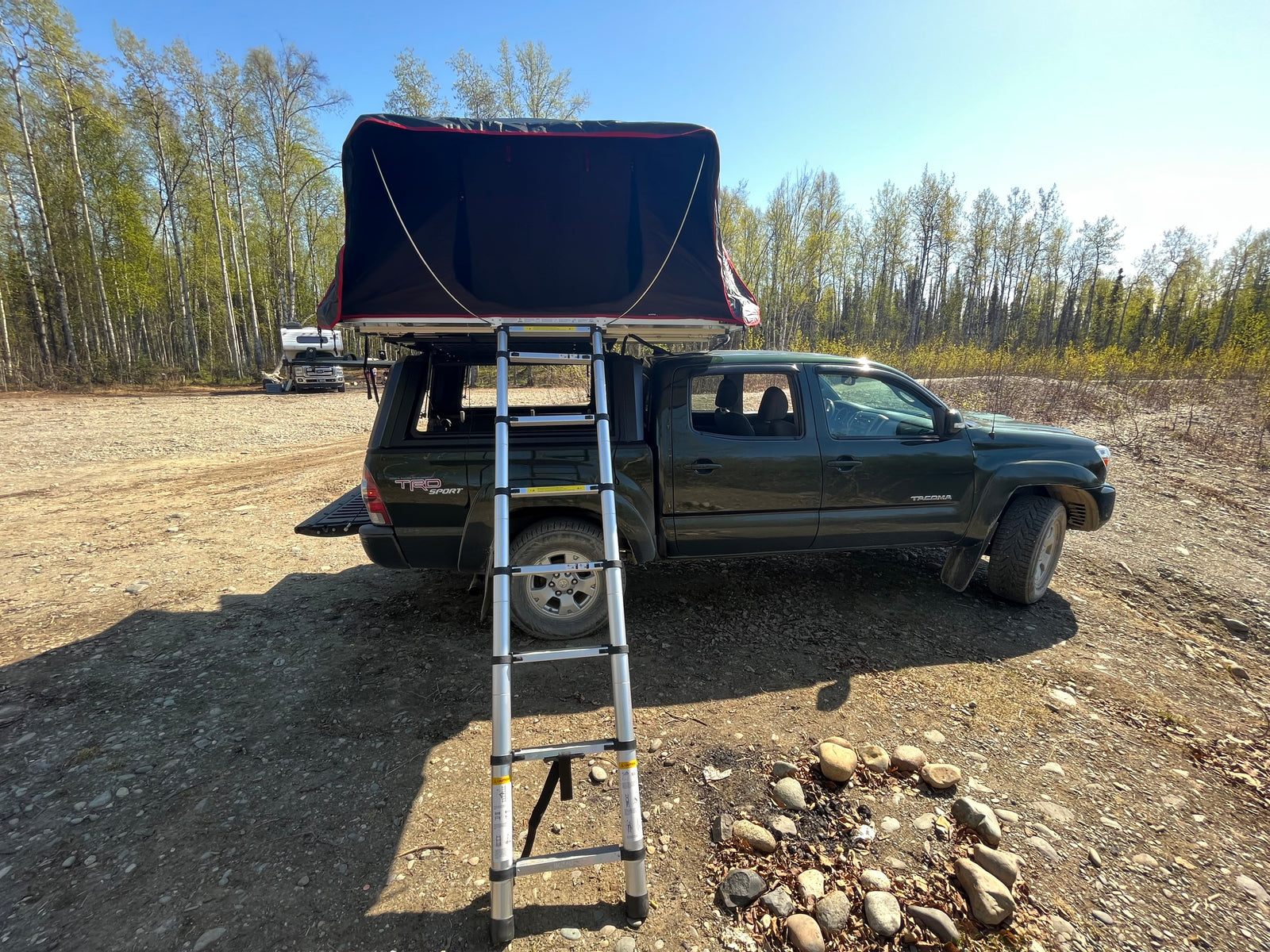 Ready for adventure: A dark green truck with a deployed rooftop tent and ladder, like an RV rental for off-grid camping.