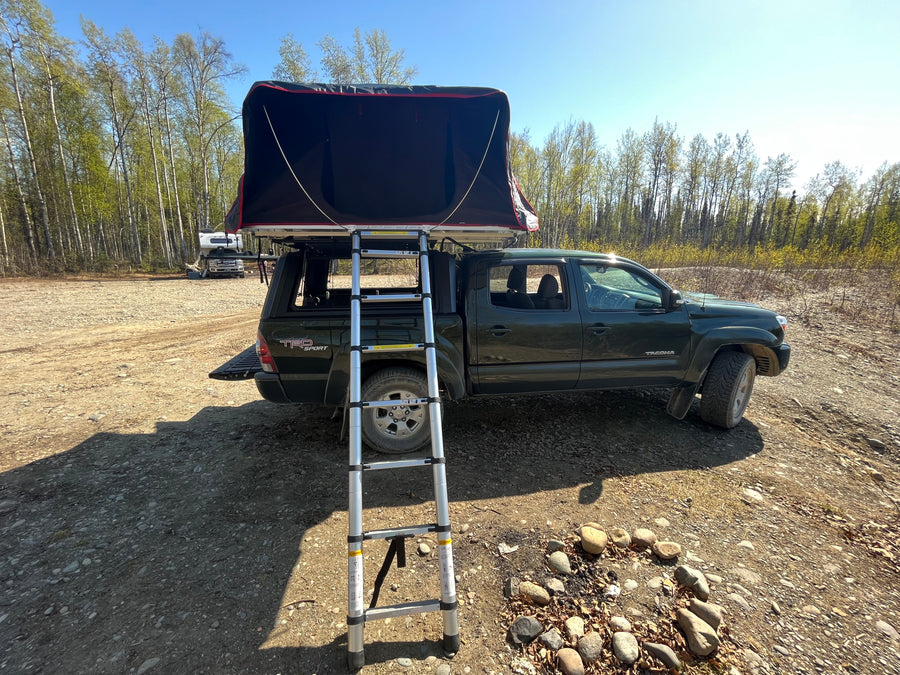Ready for adventure: A dark green truck with a deployed rooftop tent and ladder, like an RV rental for off-grid camping.