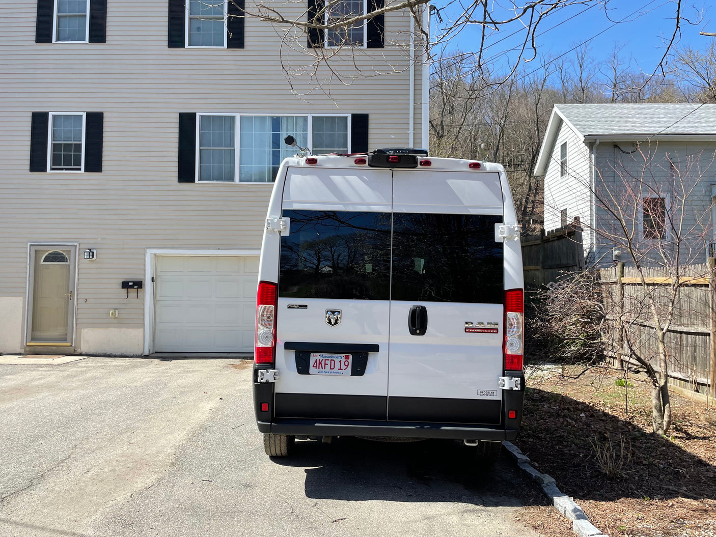 White Ram ProMaster camper van, likely an RV rental, parked on a sunny driveway beside a beige house.