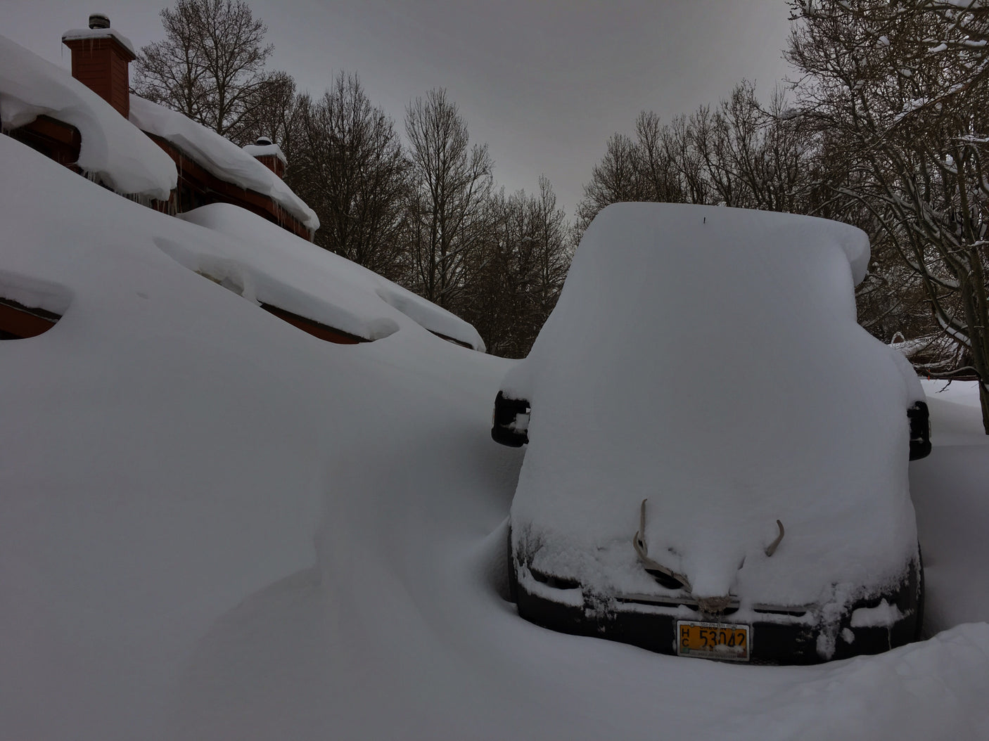 Deep snow buries a car and house roof. This extreme winter scene highlights the need for careful RV rental planning.