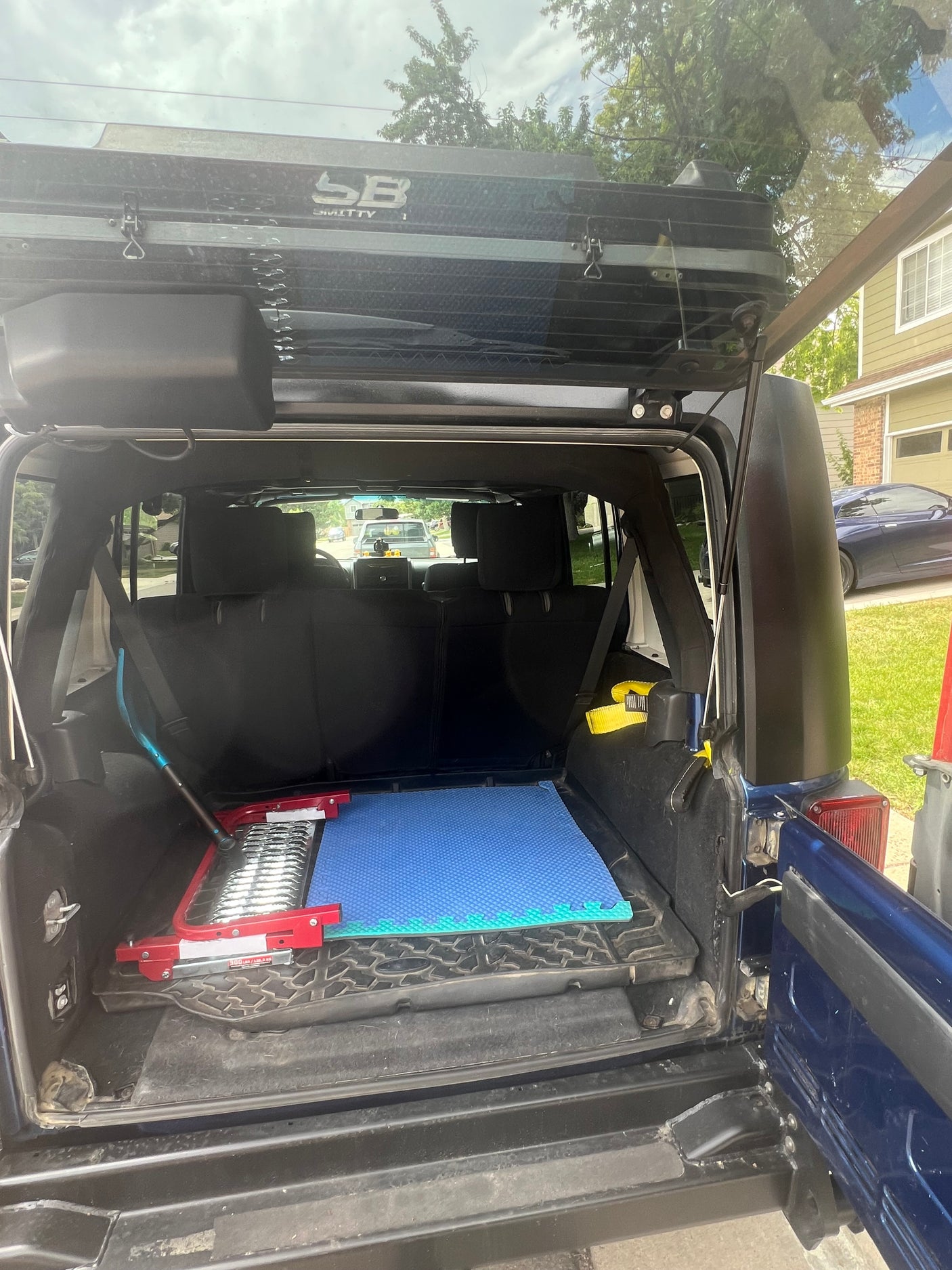 Jeep's open rear cargo area shows an overhead rooftop tent, recovery boards, and mats. Ready for adventure, like an RV rental!