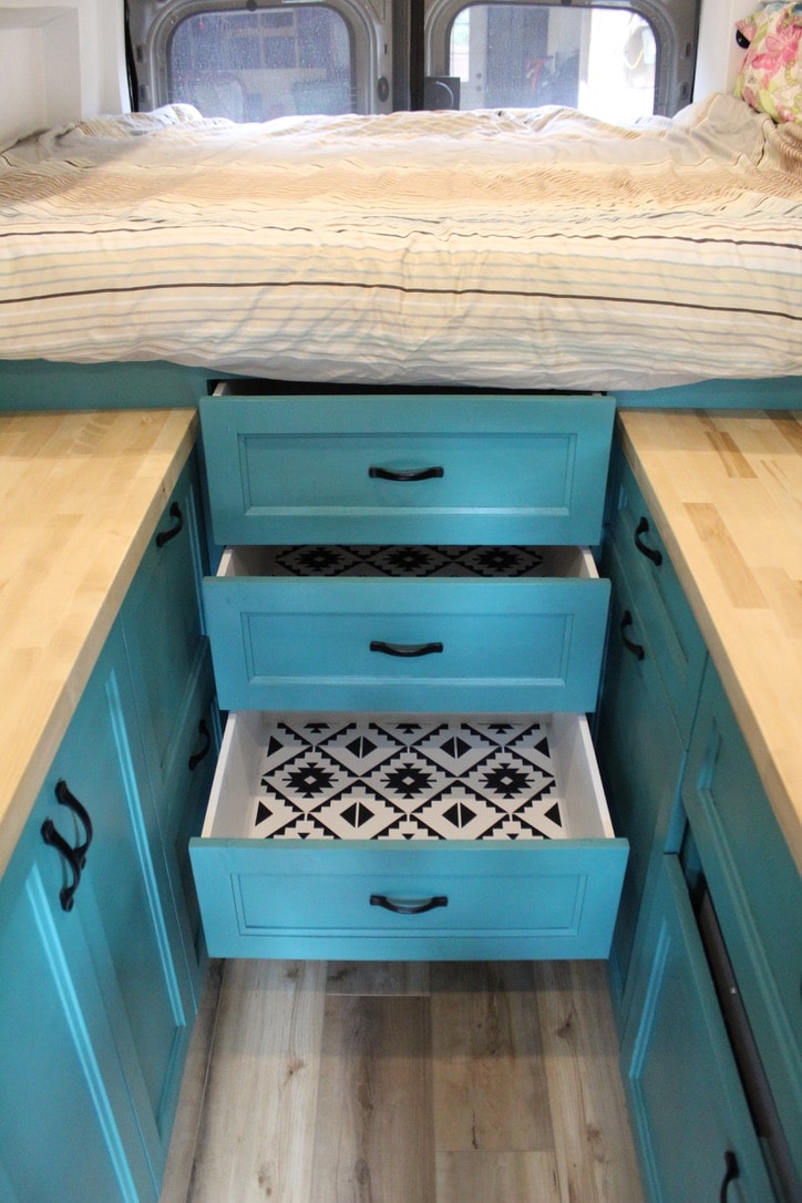 and climate control remote on a patterned wall beside a bed.|Inside an RV rental: a cozy bed with striped comforter