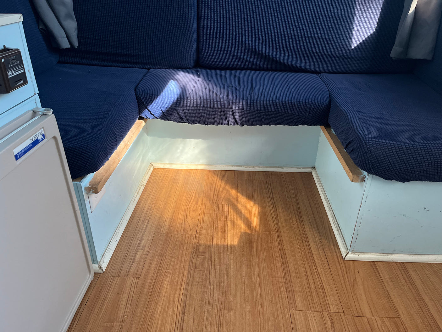 RV rental: Compact interior with blue cushioned seating, wood laminate floor, and a Norcold mini-fridge.