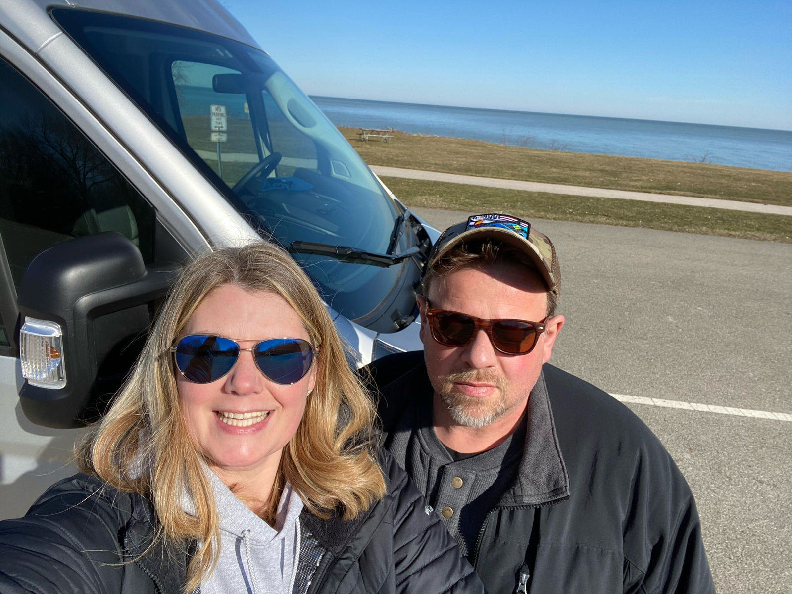 facing an open rear door with an ocean view. Shelves & controls visible.|Couple dines in a functional RV rental. Built-in bed