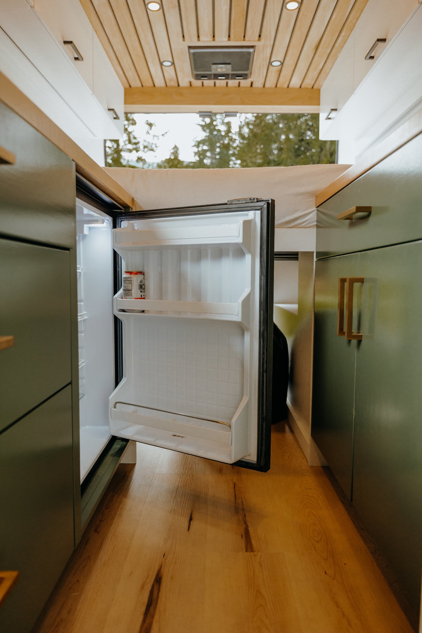 Inside this RV rental: an open mini-fridge, wood flooring, and olive green cabinets, perfect for mobile living.
