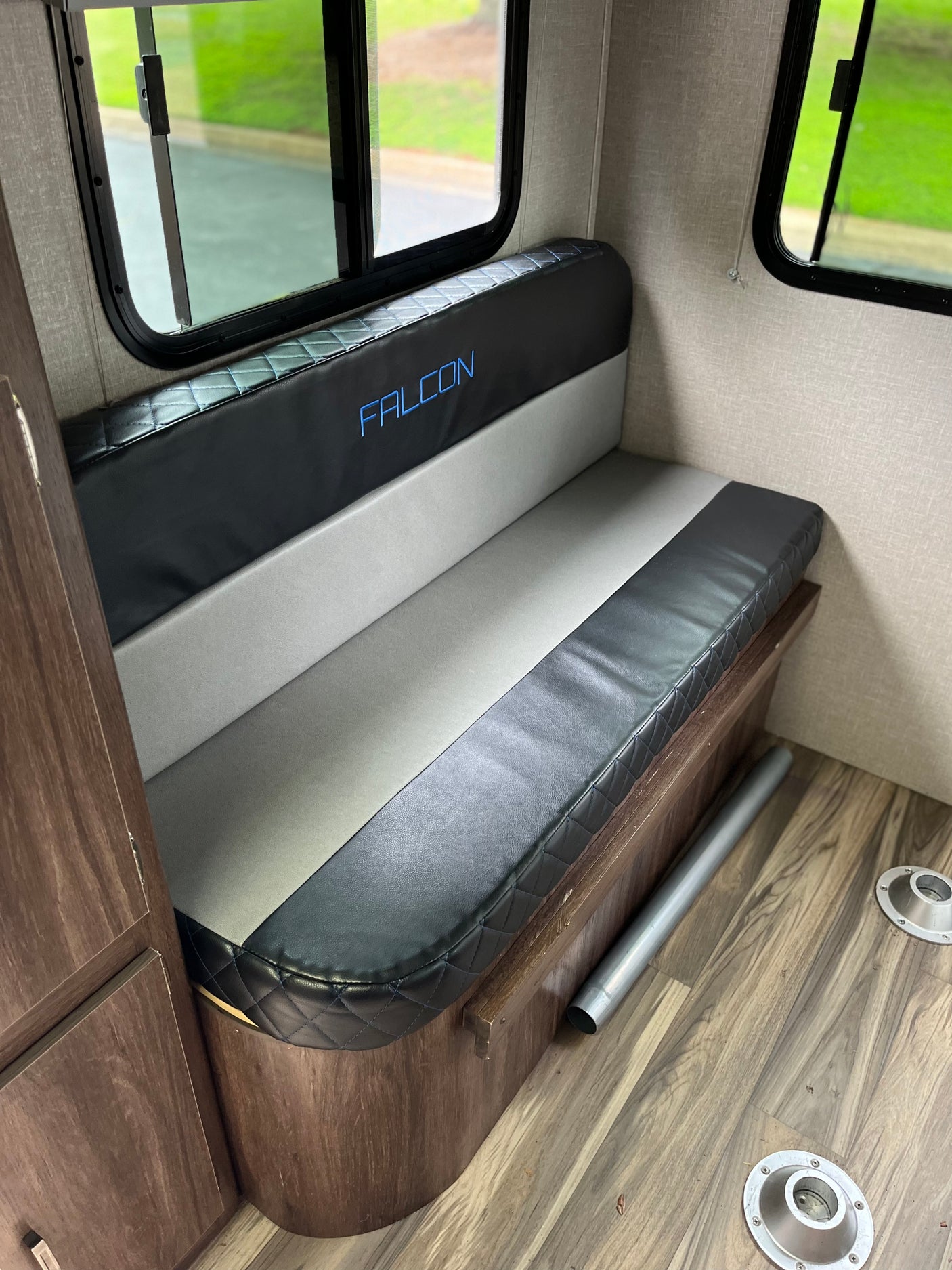 RV rental dinette with black and gray 'FALCON' bench seating, wood-look floor, table mounts, and bright windows.
