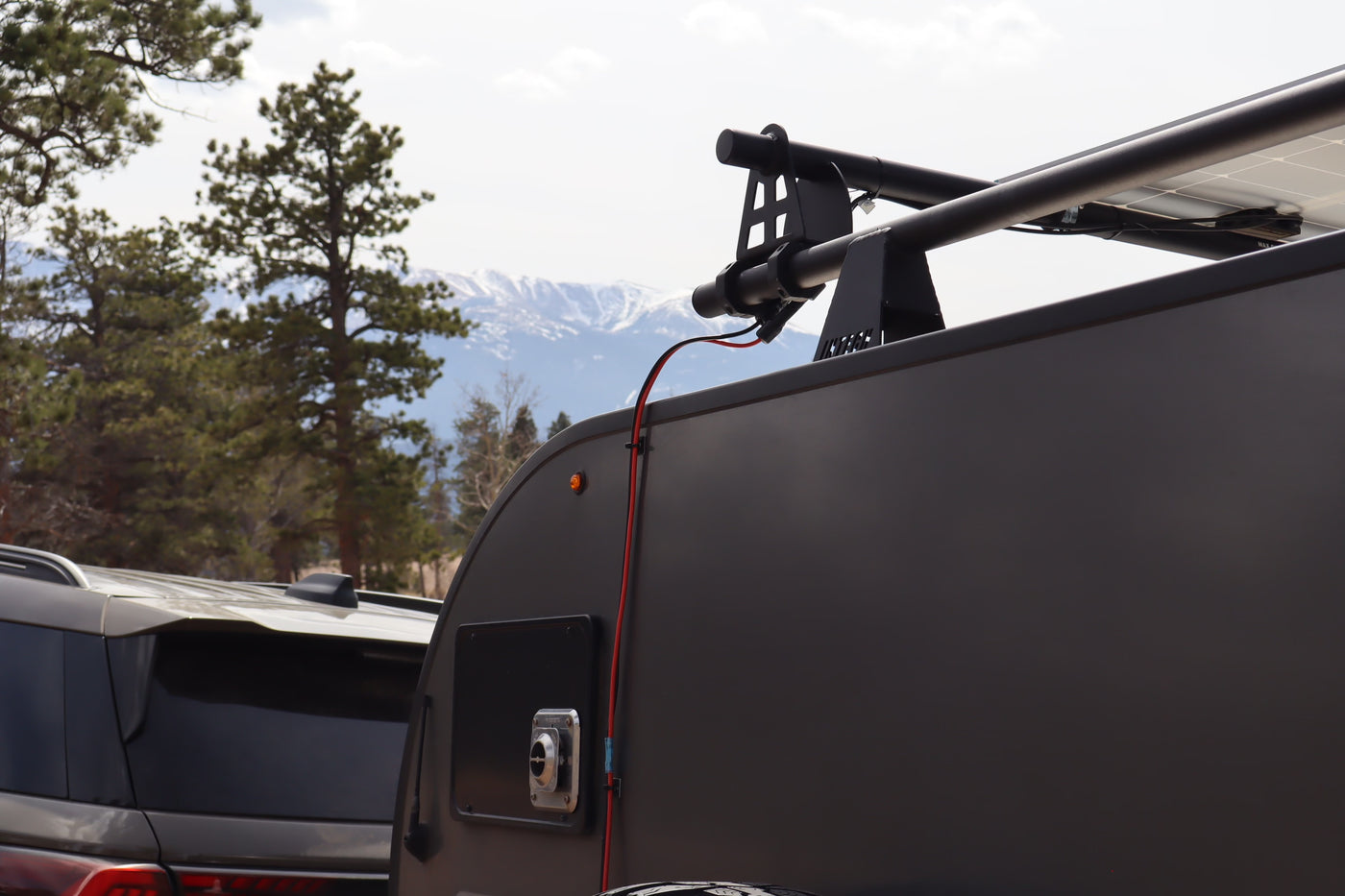 This rv rental shows a teardrop camper with solar panels, a roof rack, and an electrical hookup, set against scenic mountains. — photo 9