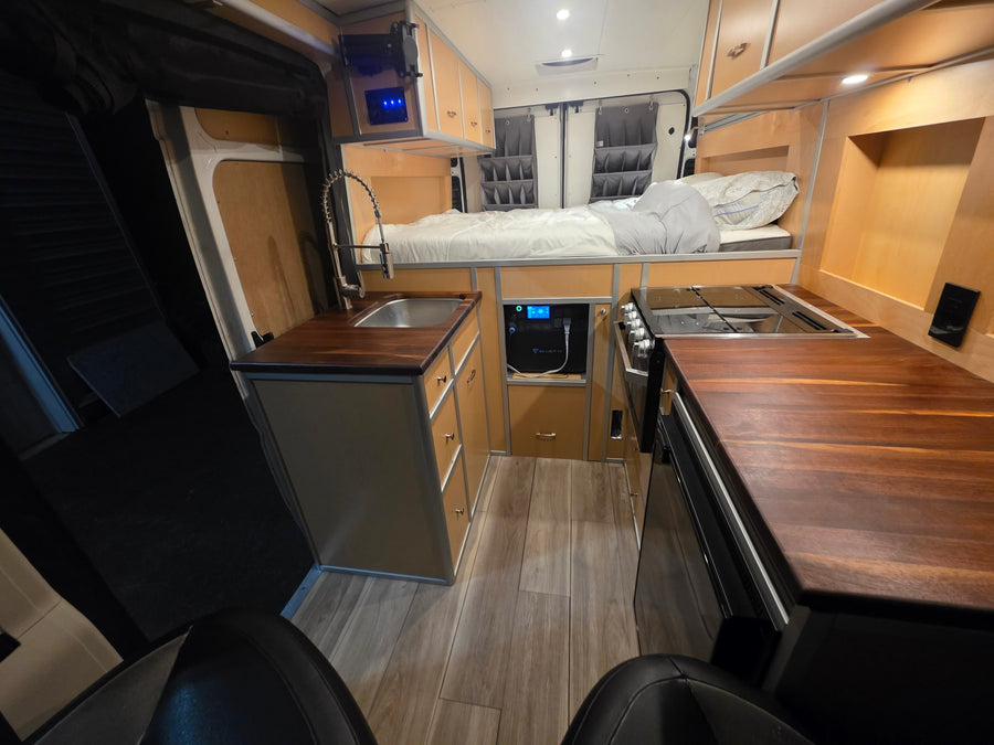 Step into this inviting rv rental featuring a full kitchen with sink, stove, wood countertops, and a comfortable bed.