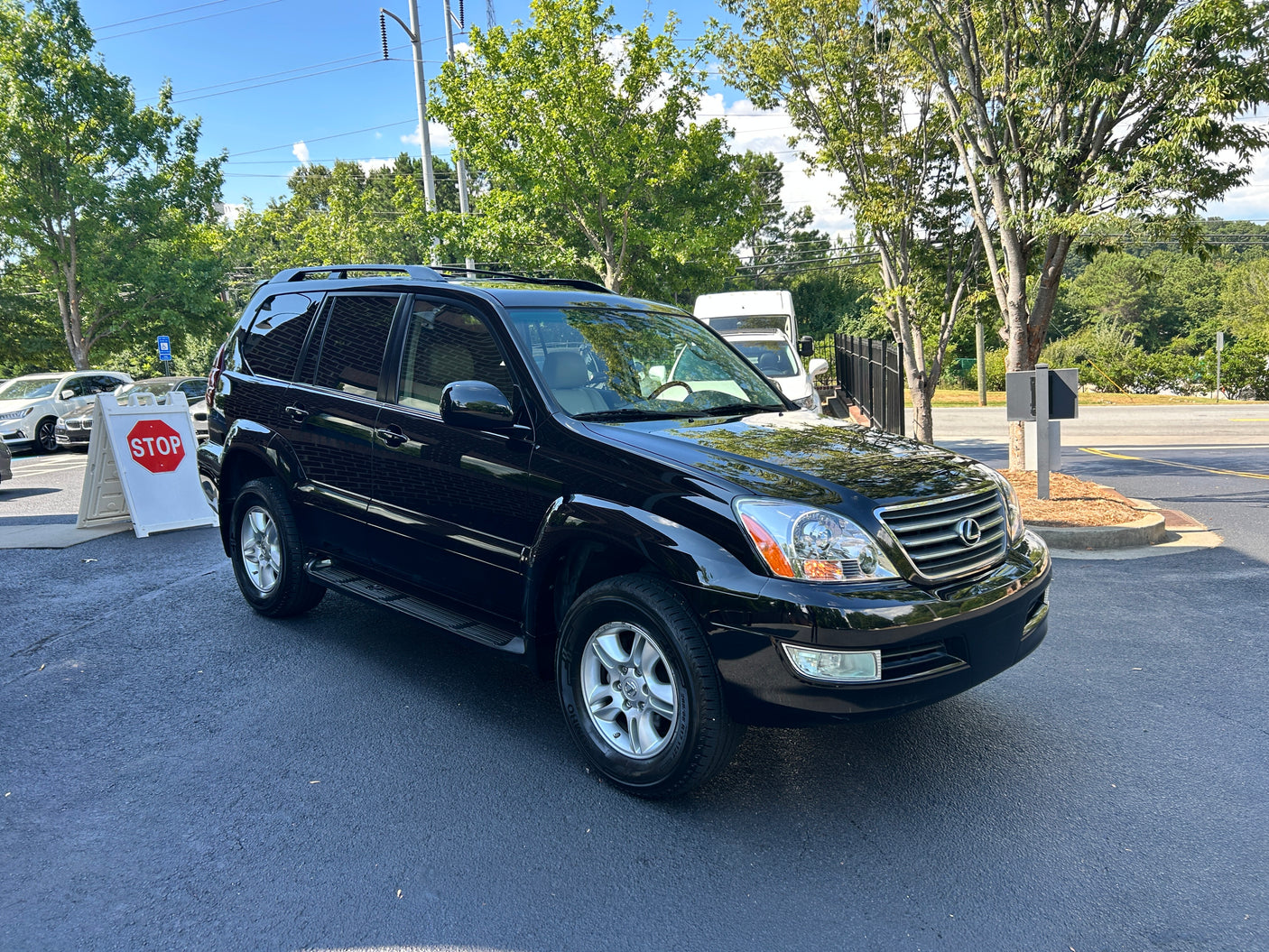 A shiny black Lexus SUV is parked on an asphalt lot, with a white van suggesting an RV rental business in the background.