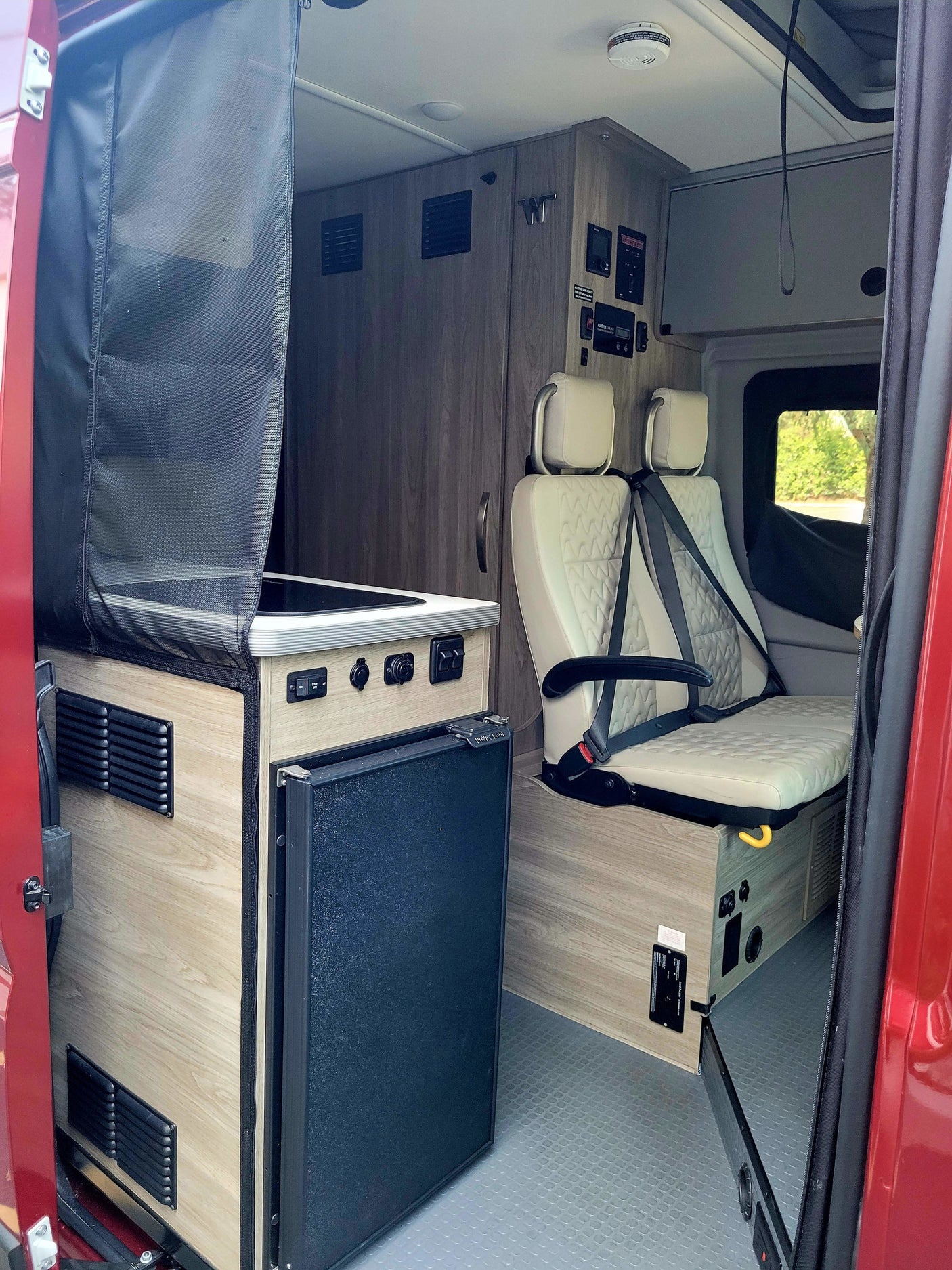 Step inside this RV rental featuring a sleek kitchenette with fridge and cozy, quilted passenger seating. Ideal for travel.