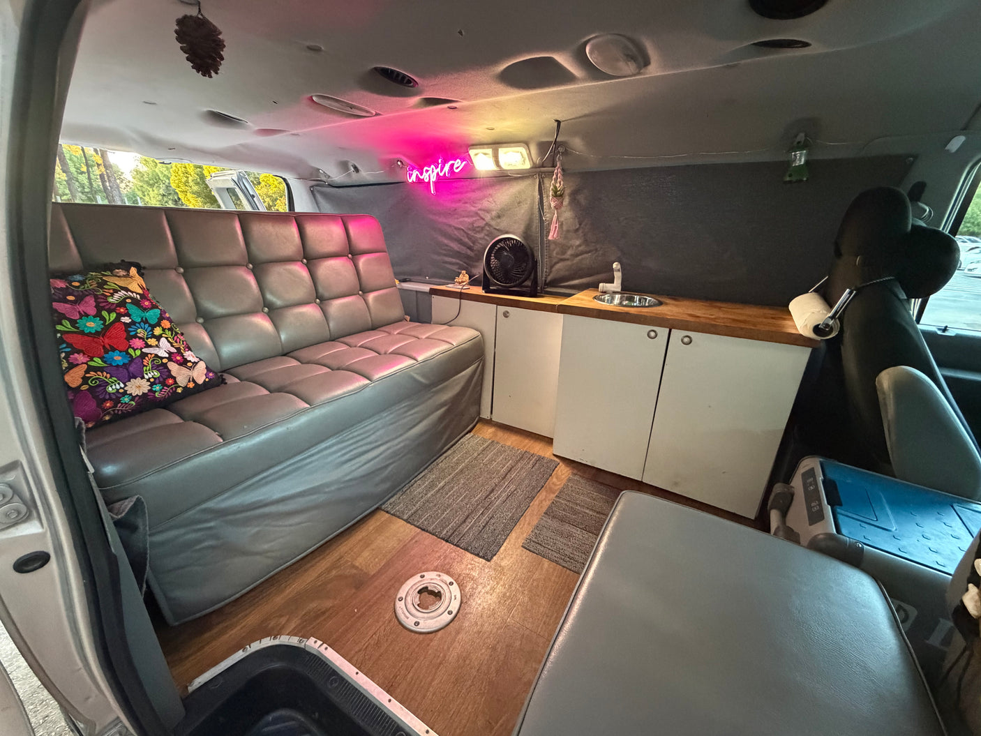 Cozy rv rental interior: gray tufted couch, wooden floors, kitchenette with sink, and a pink "inspire" neon light.