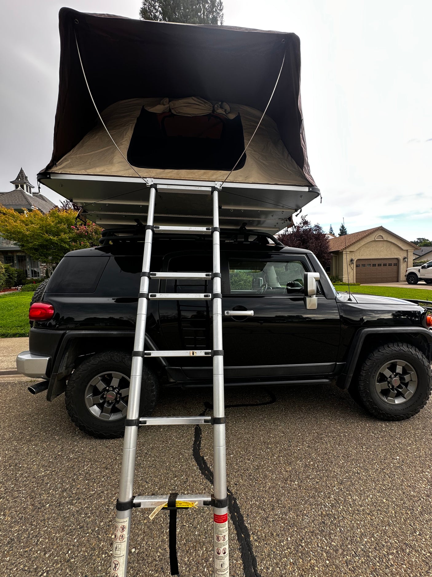 Black SUV with a deployed rooftop tent and ladder, ready for camping. A unique RV rental alternative for adventures!