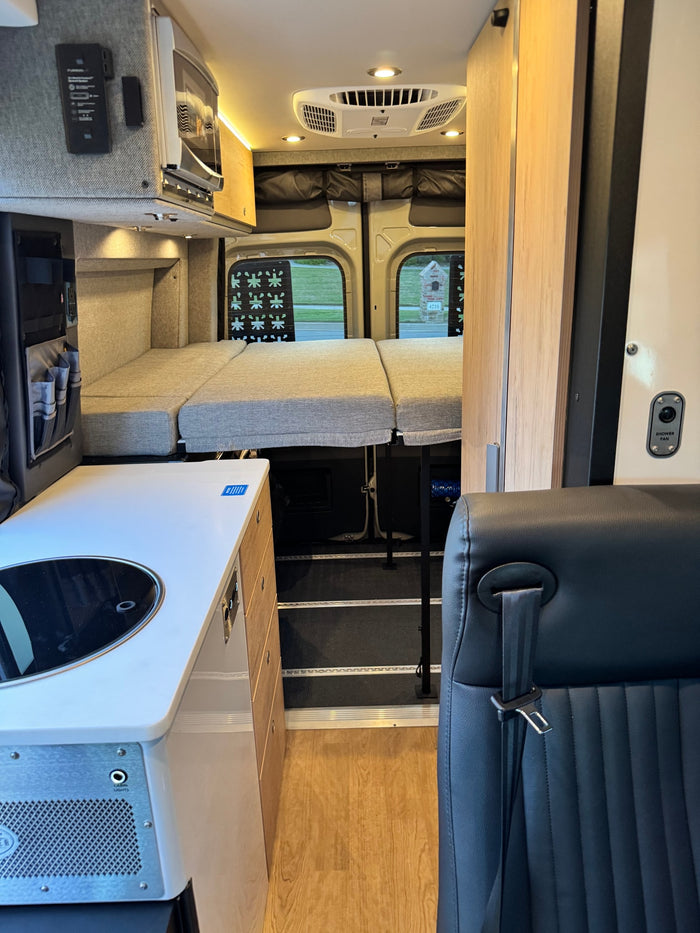 This RV rental interior features a compact kitchenette, microwave, comfortable bed, and AC, perfect for road trips.
