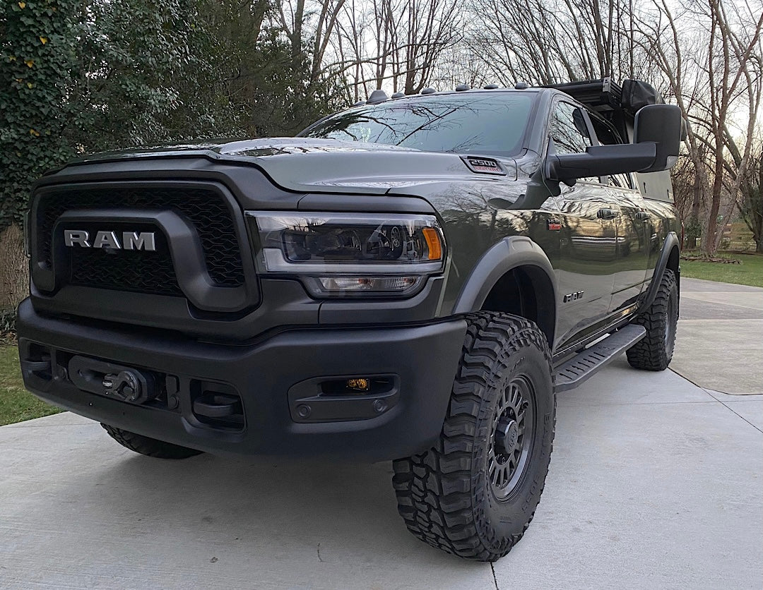 A dark green Ram heavy-duty truck, equipped with off-road tires and a front winch, seen parked outside. Ideal for an rv rental journey.