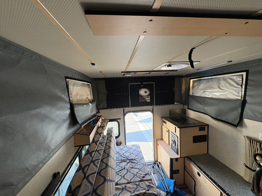 Cozy rv rental interior: patterned bench, compact kitchen, pop-top walls, and a view through the open back door.